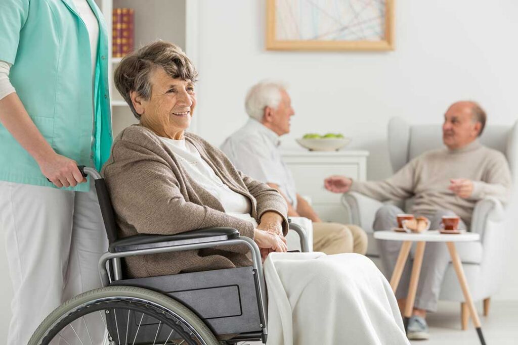 Older adult and caregiver talking quietly in a bright assisted living common room.